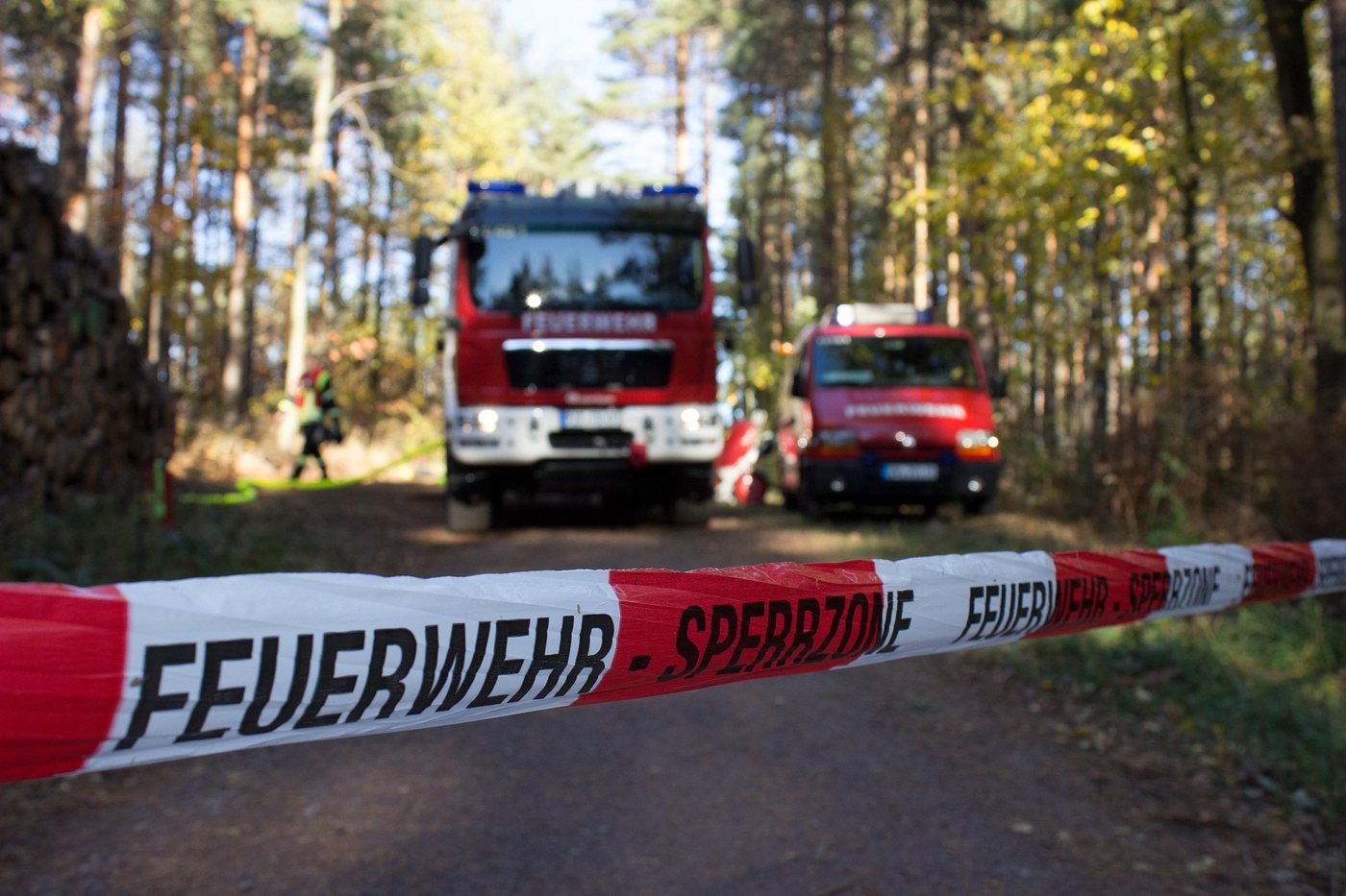 Ein Löschfahrzeug und ein kleineres Fahrzeug stehen auf einem sandigen Waldweg,
                davor ein Absperrband mit der Aufschrift Feuerwehr Sperrzone.